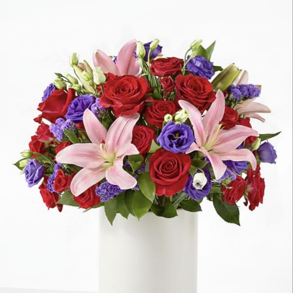 Bouquet of red roses, pink lilies, and purple blooms in a white vase