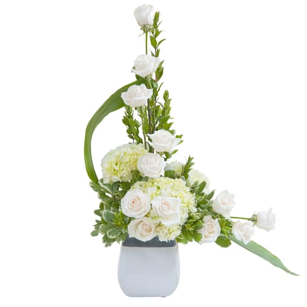 Tall white rose and hydrangea arrangement in a white square vase with an asymmetrical design
