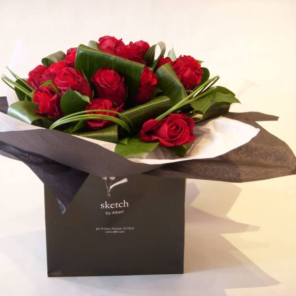 Red roses arranged in black and white wrapping inside a black gift bag