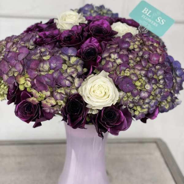 Purple and white roses with purple hydrangeas in a tall vase