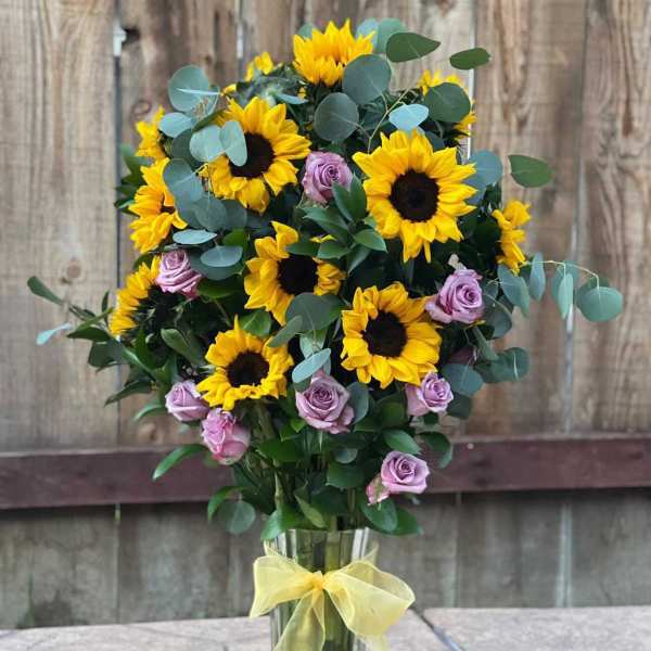 Sunflower and lavender rose bouquet in a clear vase with a yellow ribbon
