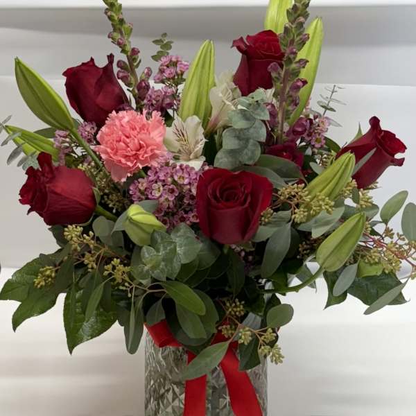 Red roses and pink flowers in a glass vase with a red ribbon