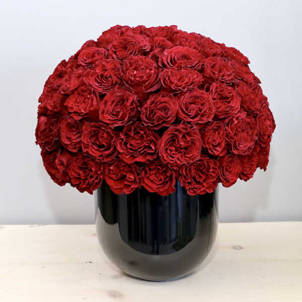 Dense dome of red roses arranged tightly in a glossy black cylindrical vase