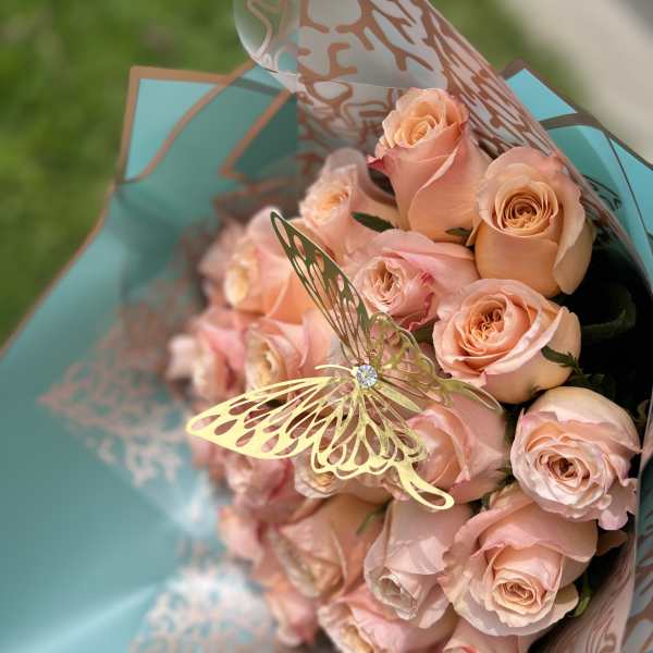 Bouquet of pale peach roses wrapped in turquoise paper with a butterfly pick
