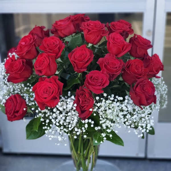 Tall arrangement of red roses with white baby's breath in a clear glass vase