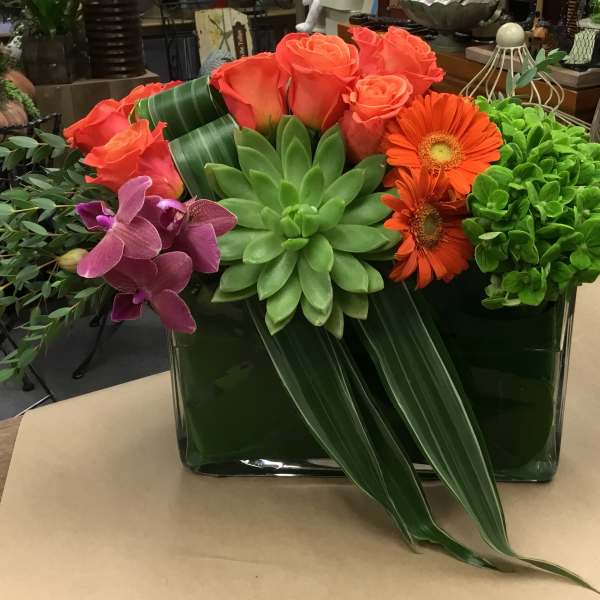 Succulent and rose arrangement with orange gerbera daisies in a glass vase