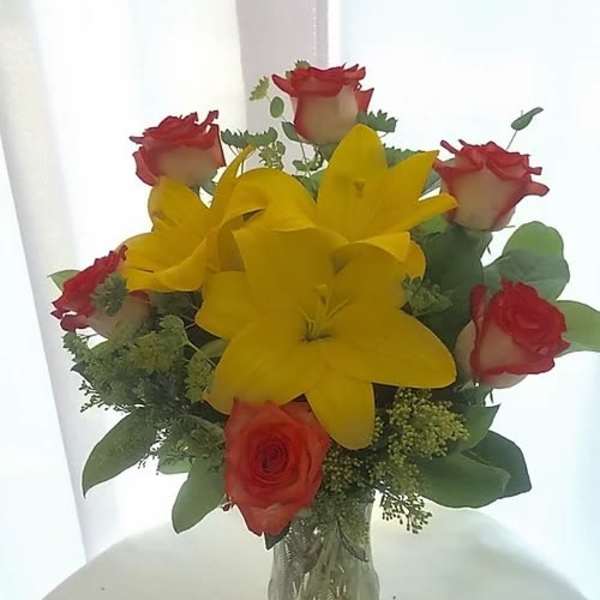 Bouquet of red roses and yellow lilies in a clear glass vase