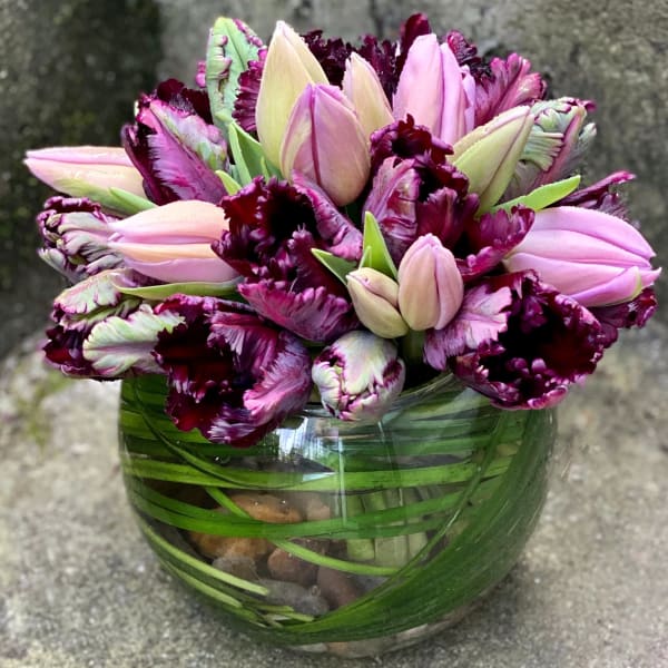 Pink and burgundy tulips clustered in a round glass vase lined with green leaves