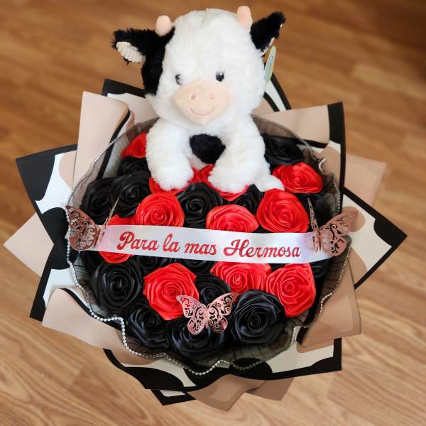 Plush cow sitting on a bouquet of red and black roses