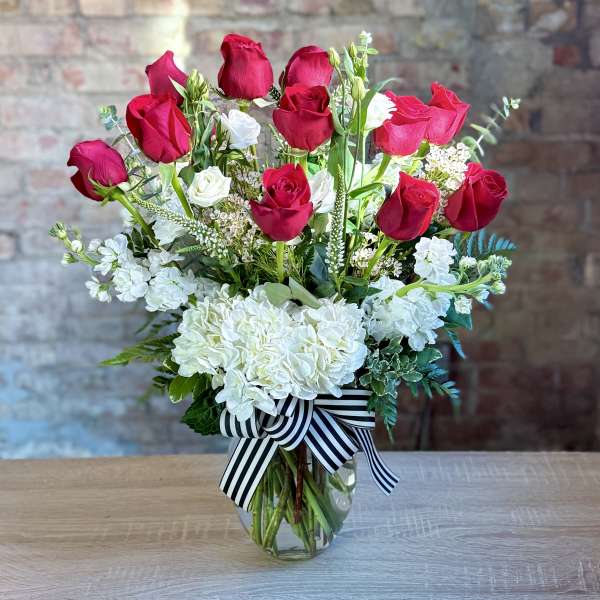 Red and white roses arranged in a glass vase with a striped ribbon