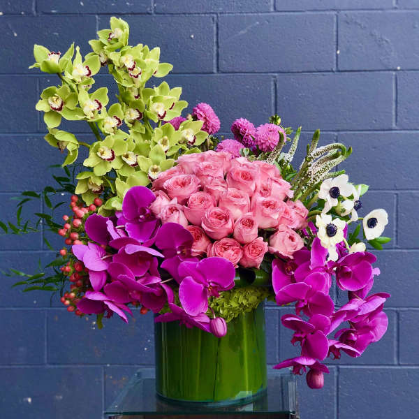 Pink roses and orchids arranged in a green glass vase