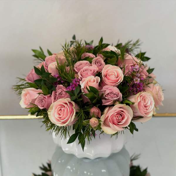 Low arrangement of pink roses with small purple blooms in a white ceramic vase