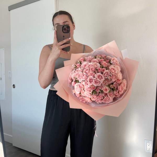 Woman holding a large bouquet of pink roses wrapped in pastel paper