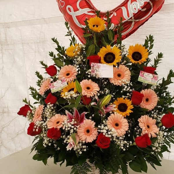 Heart-shaped red balloon above a mixed flower basket with roses and daisies