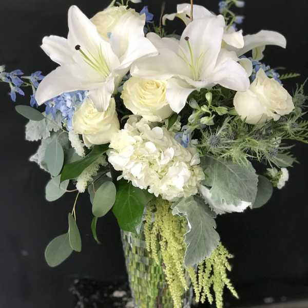 White lilies and roses in a glass vase with blue accents