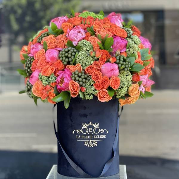 Large bouquet of orange and pink roses in a navy hatbox
