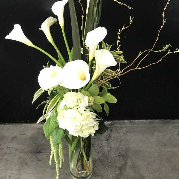 Tall arrangement of white calla lilies and hydrangea in a clear glass vase