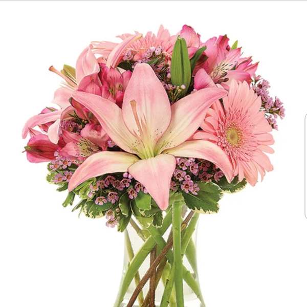 Pink lilies, gerbera daisies, and mixed blooms arranged in a clear glass vase