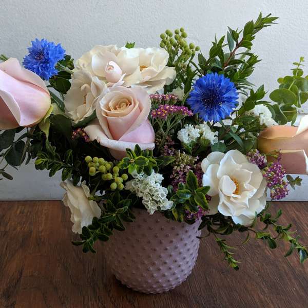 Mixed bouquet of pale roses, white blooms, and blue flowers in a textured vase