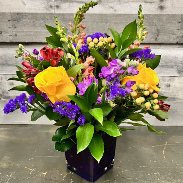 Mixed bouquet with yellow roses and purple flowers in a dark vase