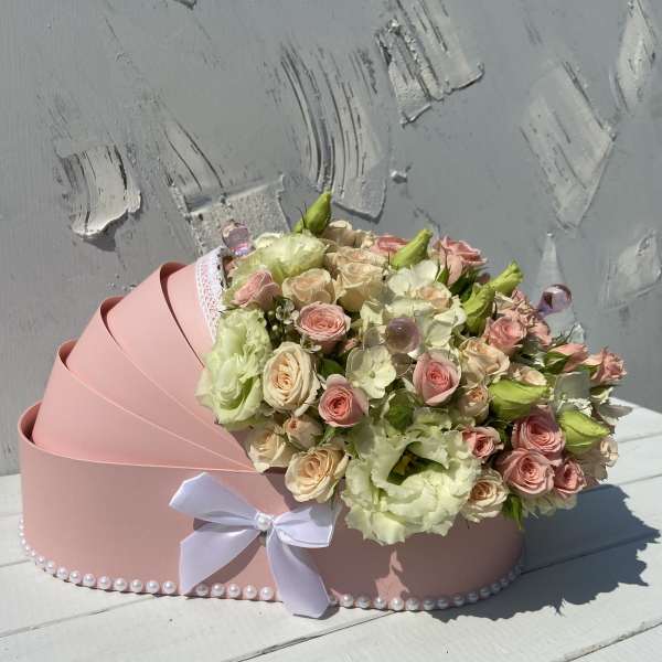 Pink carriage-shaped box filled with cream and blush roses and lisianthus, trimmed with a white bow and pearls