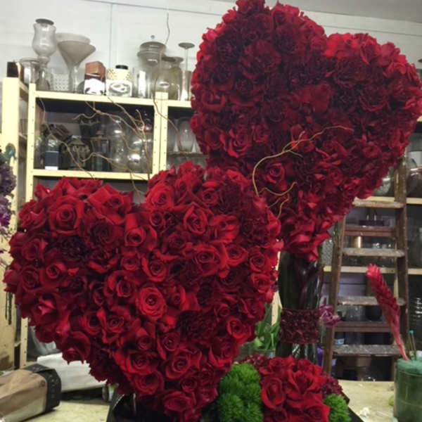 Two large heart-shaped red rose arrangements on a black base