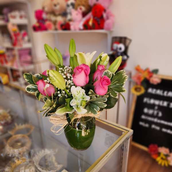 Pink roses and white lilies arranged in a green glass vase