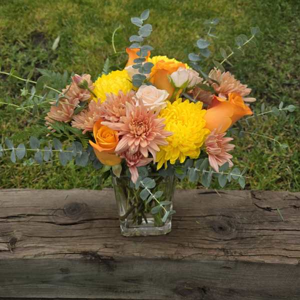 Bouquet of orange, yellow, and blush flowers in a clear glass vase