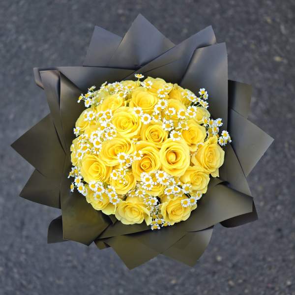 Bouquet of yellow roses with small white daisies in dark wrapping