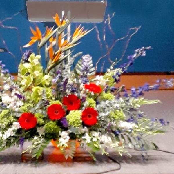 Large altar arrangement with red gerberas, orange birds of paradise, and purple flowers in a low container