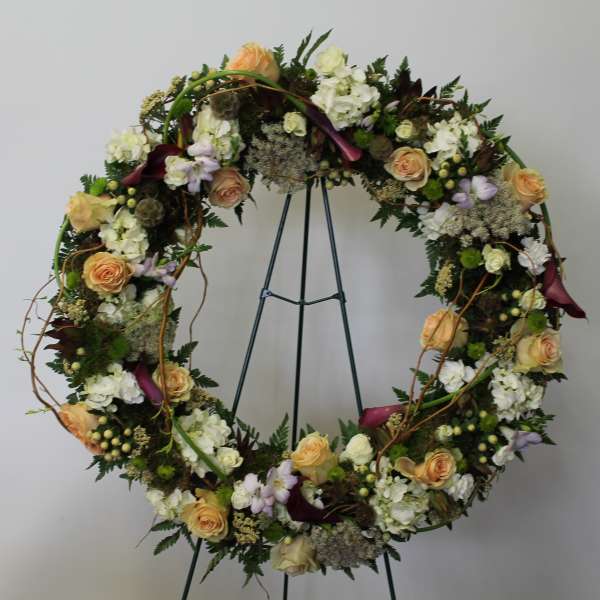 Standing wreath of peach roses, white hydrangeas, and dark calla lilies on a metal easel