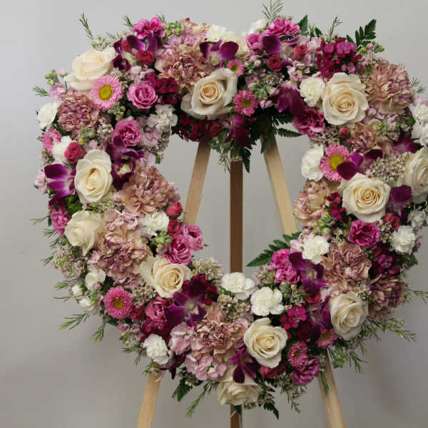 Heart-shaped wreath of cream roses and pink flowers on a wooden easel stand