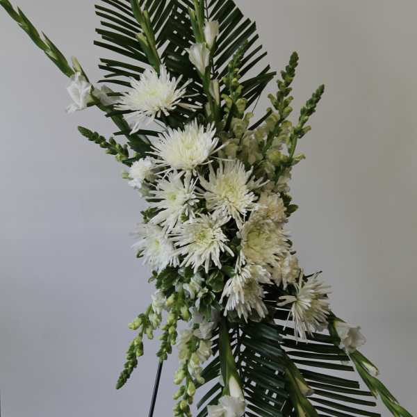 Tall white floral standing spray with mums and other blooms on an easel with large palm leaves.