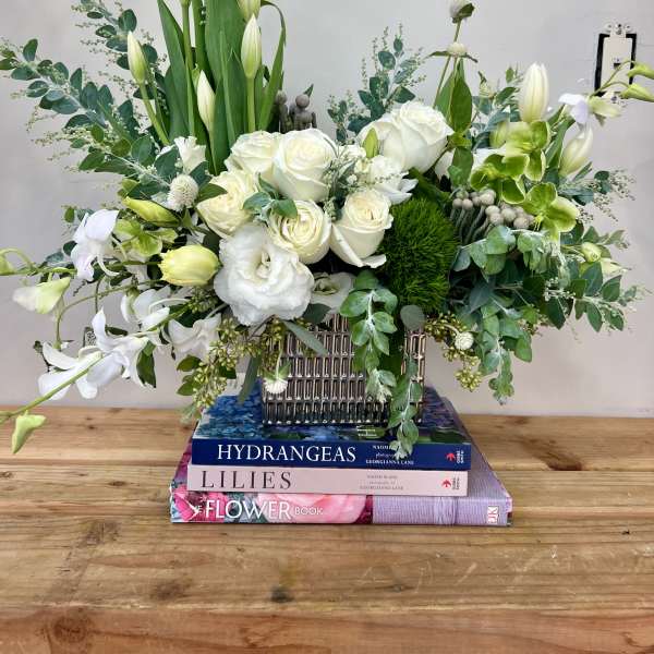 White roses and lilies arranged in a silver vase with green foliage