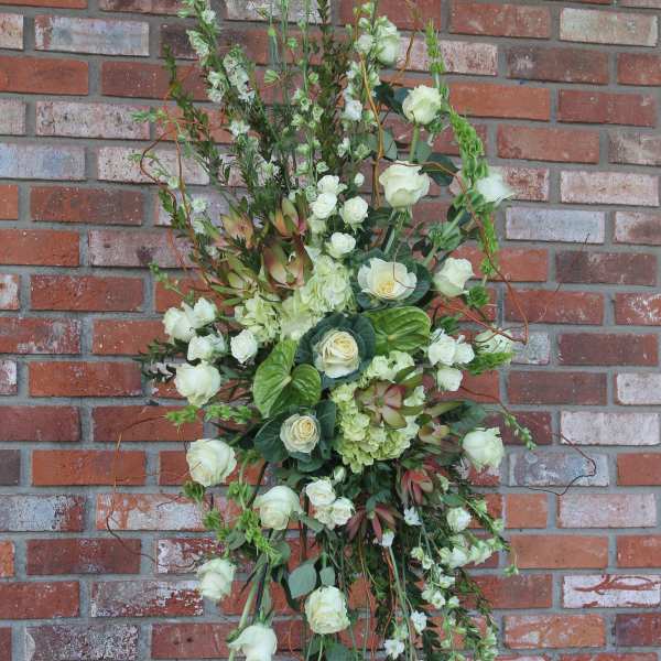 Tall standing spray of white roses and green blooms arranged on an easel against a brick wall