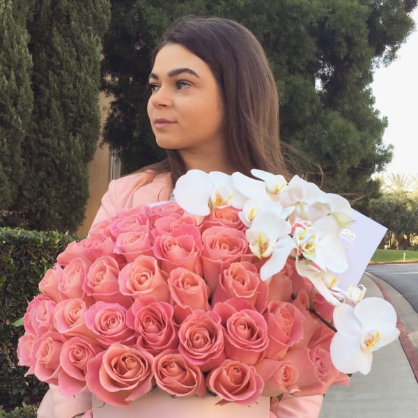 Large round pink hatbox of pink roses with white orchids, held by a person outdoors