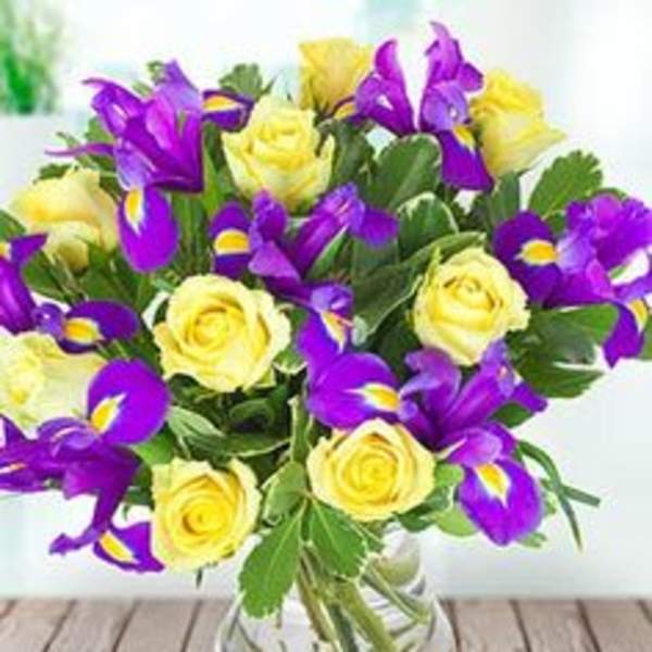 Yellow roses and purple irises in a clear glass vase