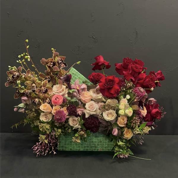 Mixed bouquet of red and blush roses with orchids in a green container