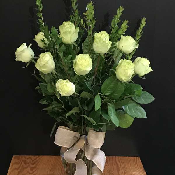 White roses arranged in a clear glass vase with a beige ribbon