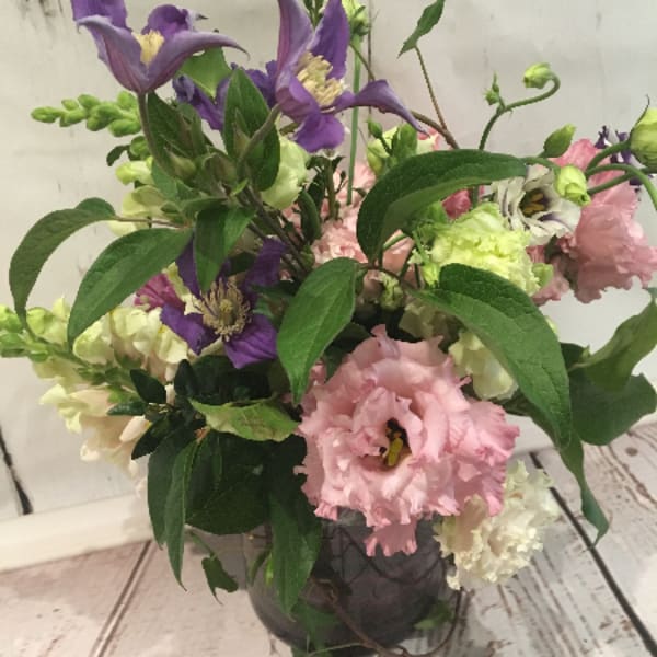Loose garden-style arrangement of purple and pink flowers in a round glass vase