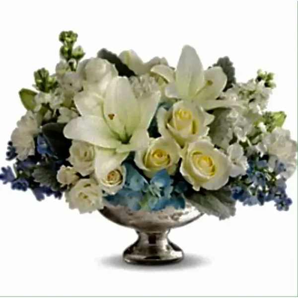 Low white lily and rose arrangement with blue accents in a silver pedestal bowl