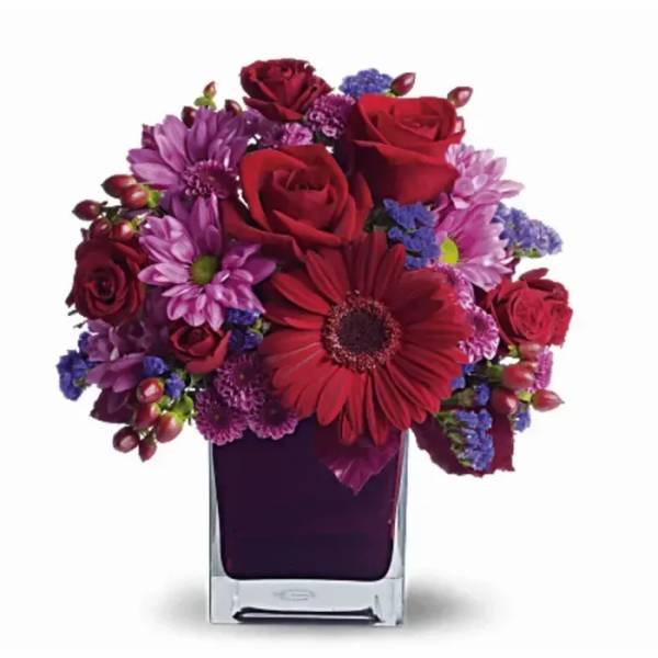 Compact mix of red roses and gerbera with purple and pink daisies in a square glass vase