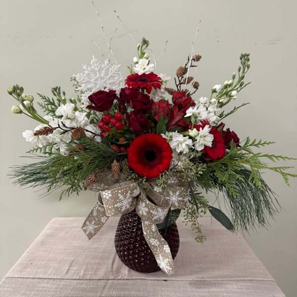 Red and white floral arrangement in a dark vase with a snowflake ribbon