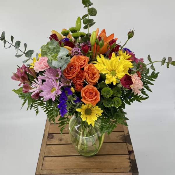 Mixed bouquet of roses, lilies, and daisies in a glass vase