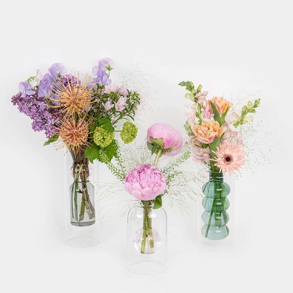 Three floral arrangements in glass vases with pink, purple, and peach blooms
