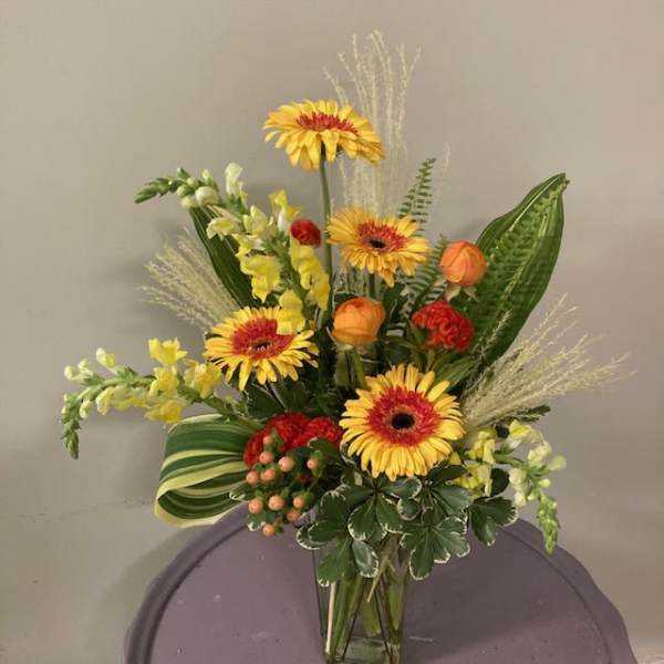 Mixed floral arrangement with yellow gerbera daisies and orange blooms in a glass vase