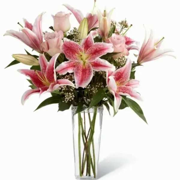 Tall glass vase of pink lilies and roses with white filler flowers.