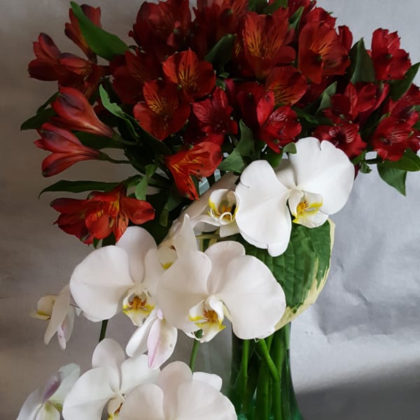 Bouquet of red alstroemeria and white orchids in a green glass vase