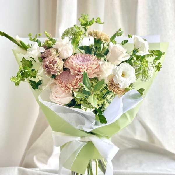 Pastel bouquet of pink chrysanthemums, pale roses and white blooms wrapped in green and white paper with a bow