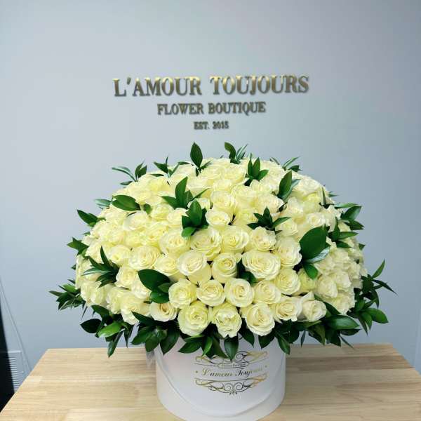 Large round hatbox of creamy white roses with dark green accents on a wooden table